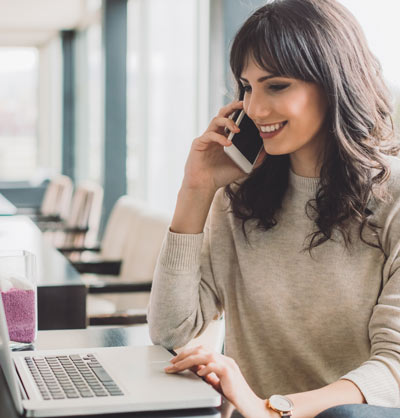 A woman working on her laptop while talking on a cell phone