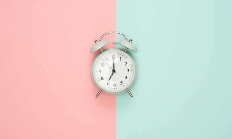 Old-fashioned silver alarm clock at 7:00 against a pink and blue background