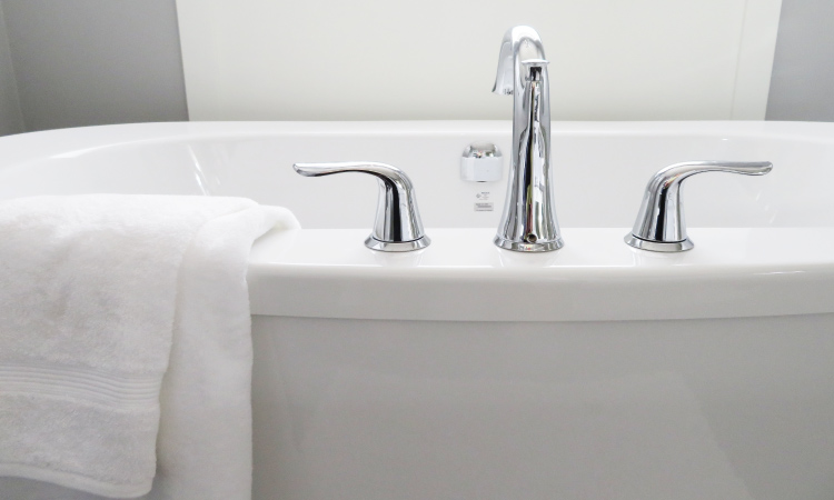Closeup of a white bathtub with a silver faucet with a white fluffy towel draped over the side
