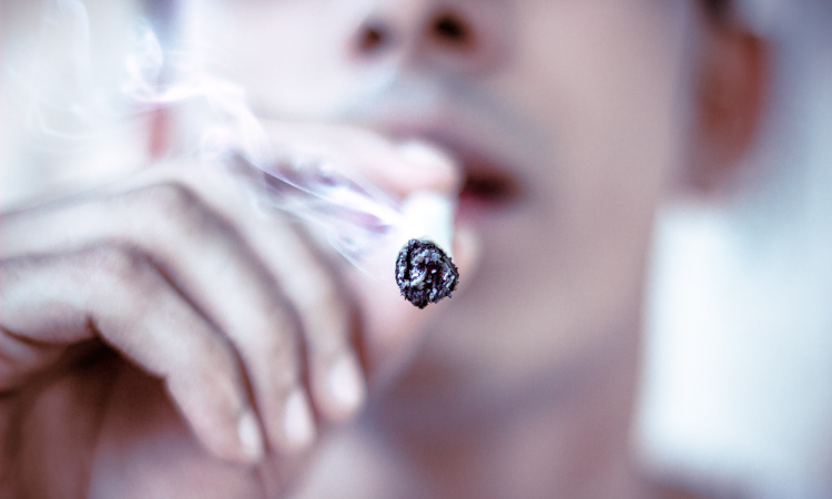 Closeup of a man smoking a dangerous cigarette that will cause bad breath and tooth discoloration